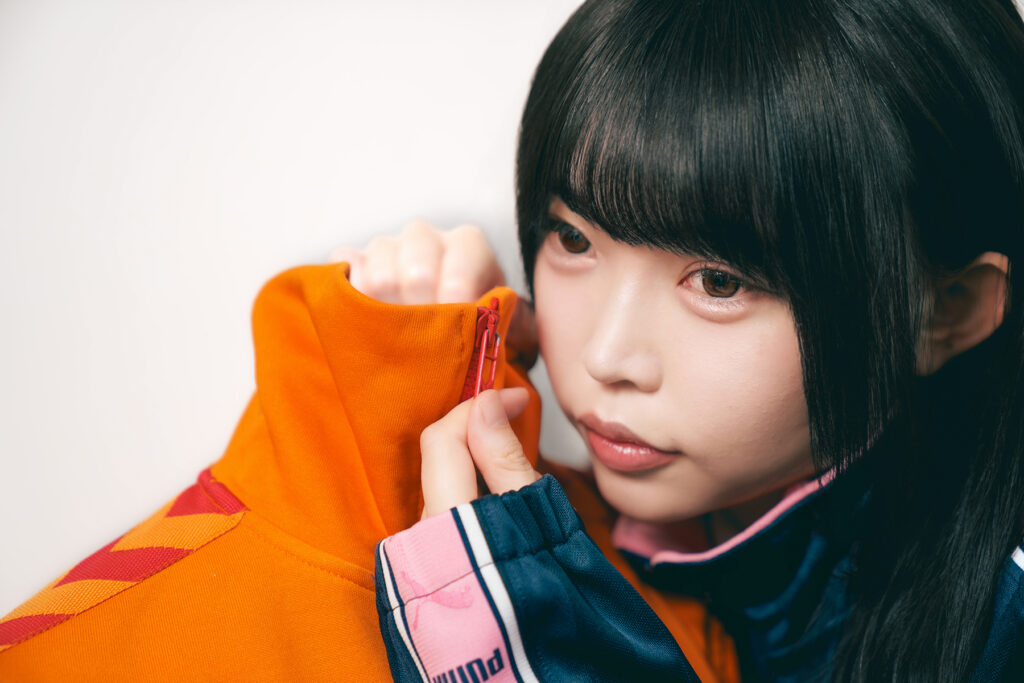 the model holding the torso, both zipped to the same collar line, her eyes elsewhere, both faces equally blank